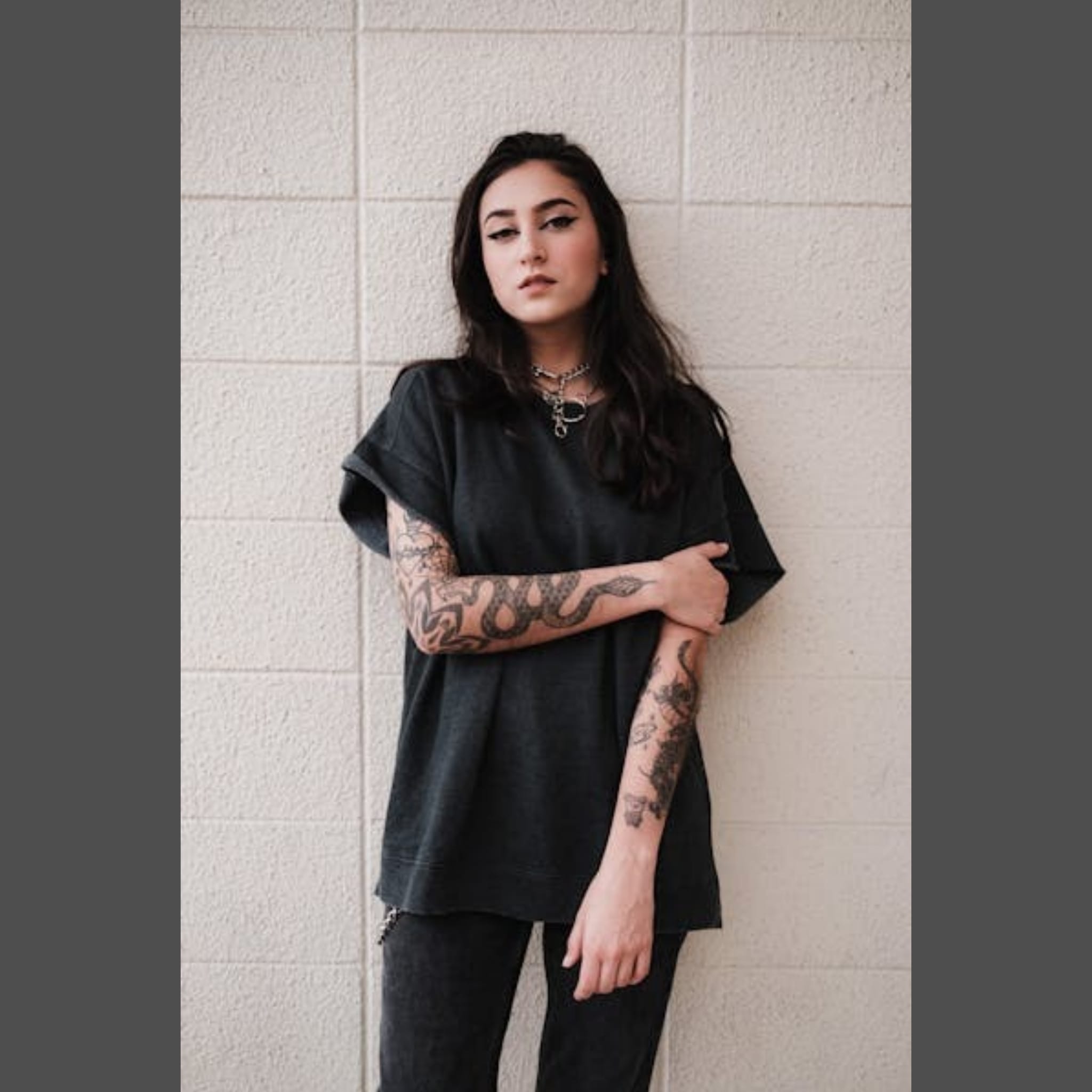 Woman in black t-shirt and jeans showing her tattooed arms