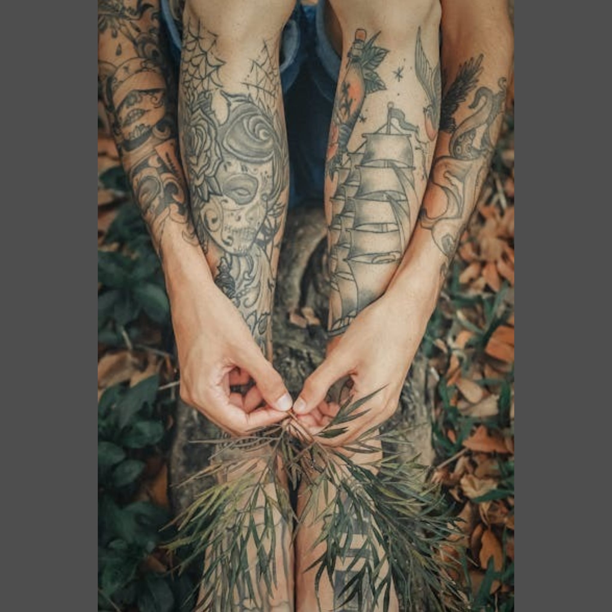 Woman sat on autumn leaves showing greywork tattoos on legs, feet and arms 