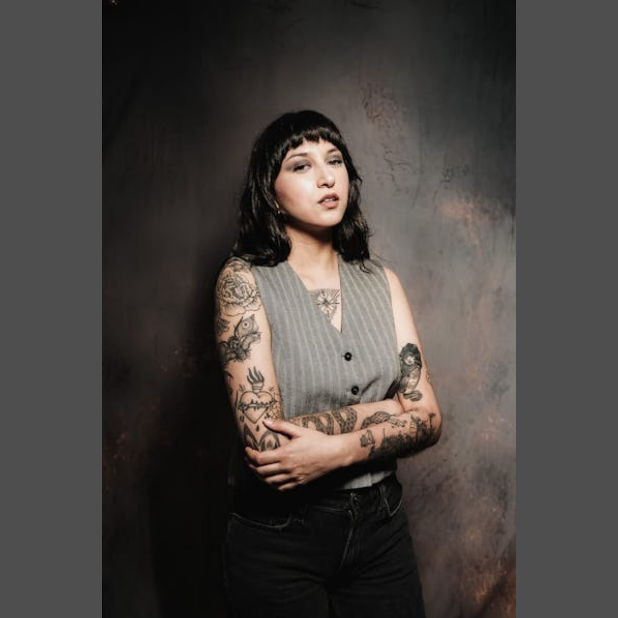 Woman in pinstripe vest showing the black tattoo work on her arms
